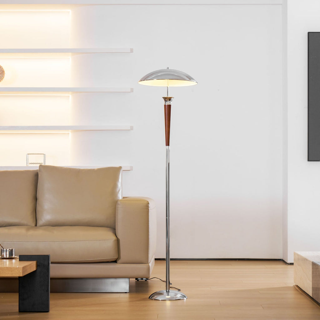 Clérachic floor lamp standing with a walnut stem and chrome pole stands in a bright room with a tan leather sofa and glowing wall shelves.