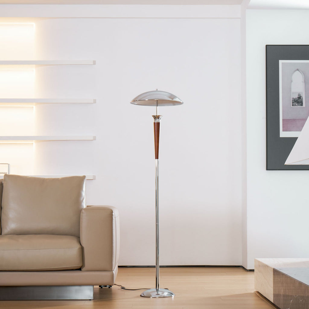 Room view of a Clérachic floor lamp with a chrome dome stands beside a beige leather sofa, with wall shelves glowing behind it.