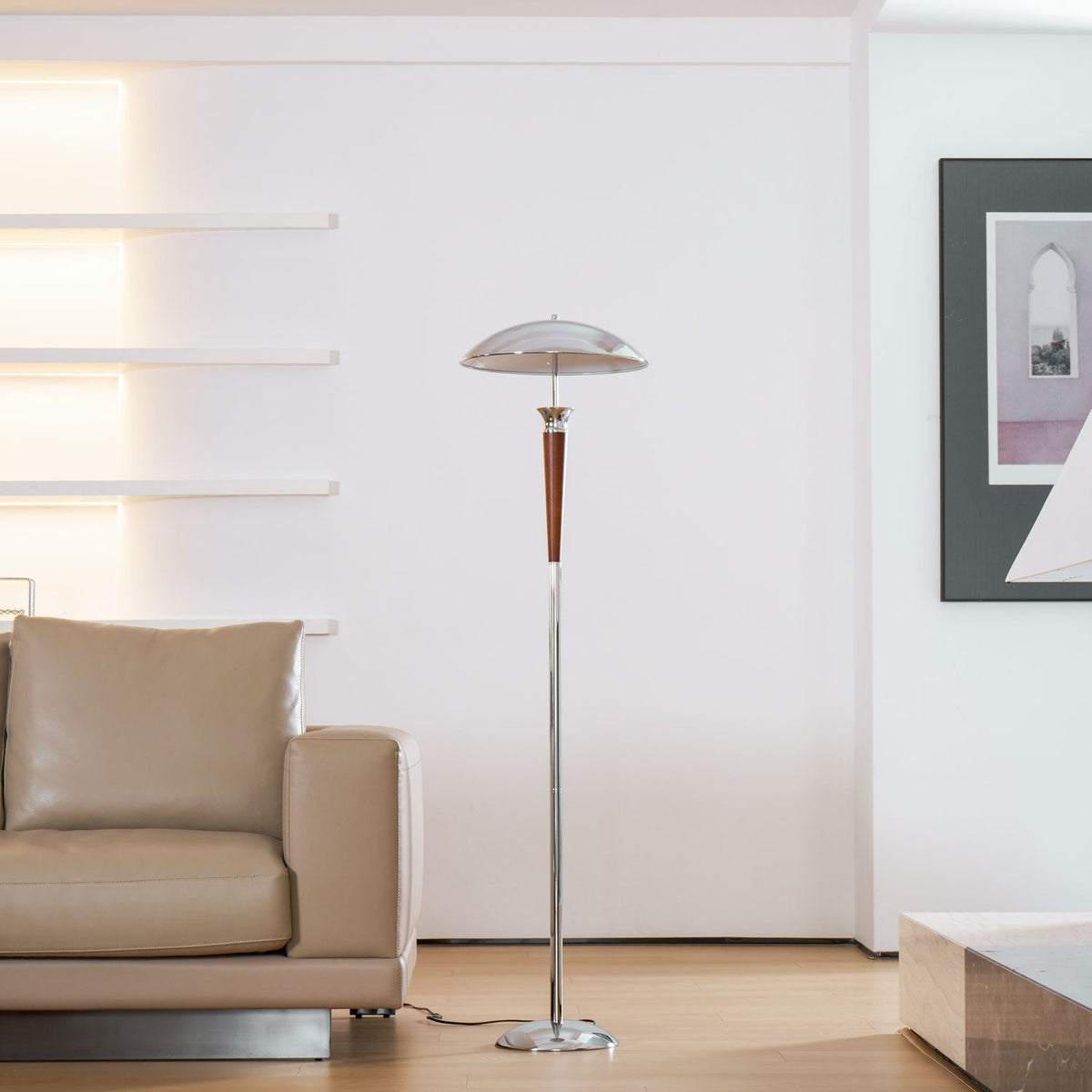 Room view of a Clérachic floor lamp with a chrome dome stands beside a beige leather sofa, with wall shelves glowing behind it.