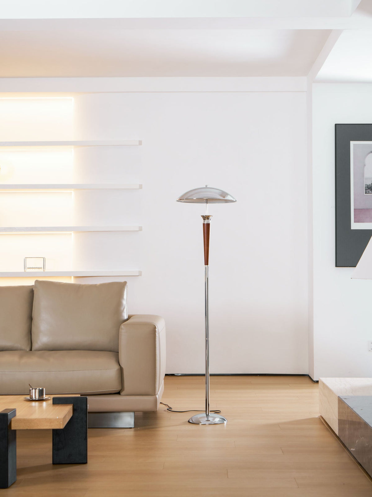 A Clérachic floor lamp stands in a pale living room by a tan leather sofa, with a low wooden table and a framed print.
