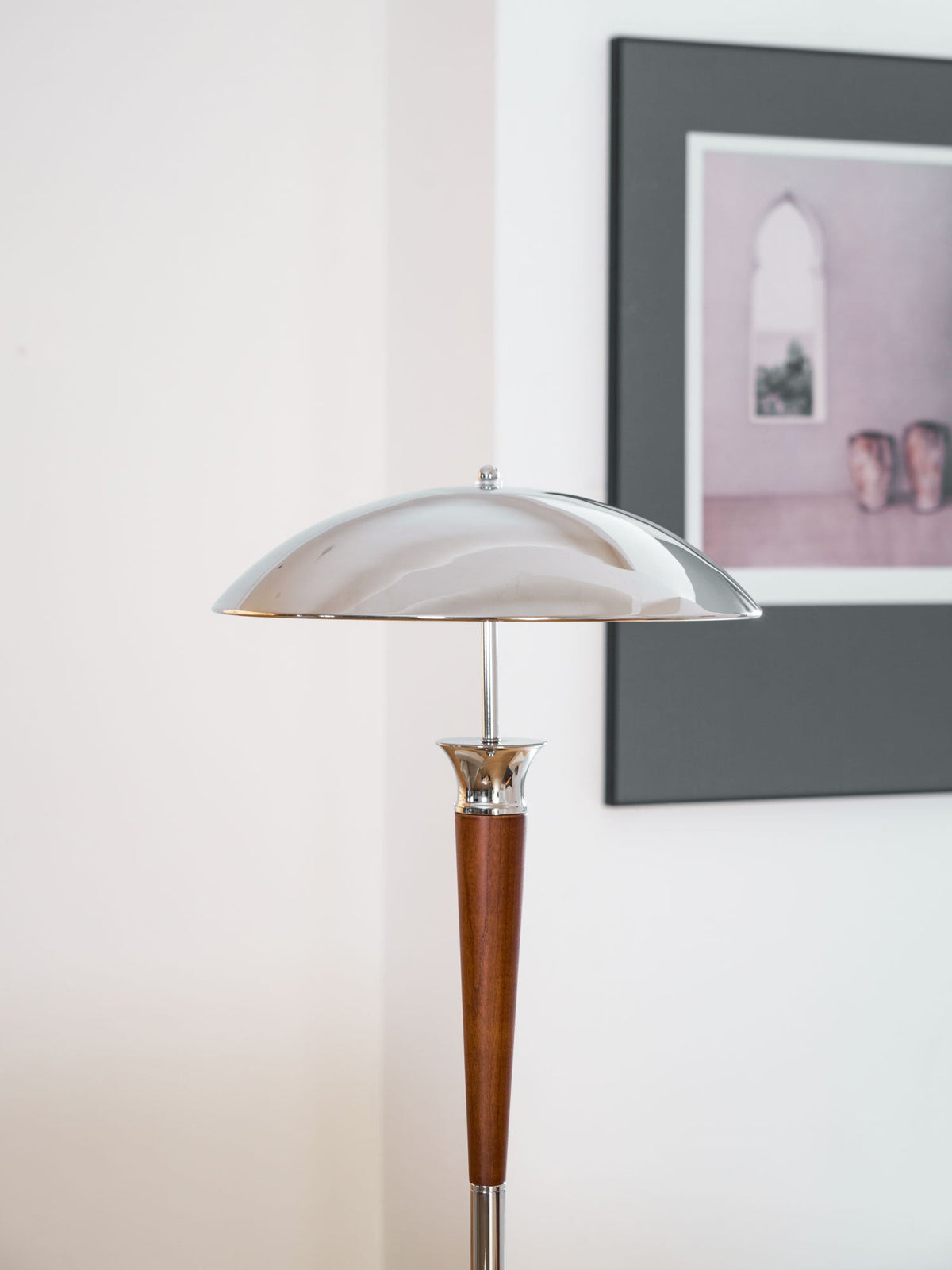 Close view of the chrome dome shade and walnut stem on this Clérachic floor lamp, in front of a dark framed print.