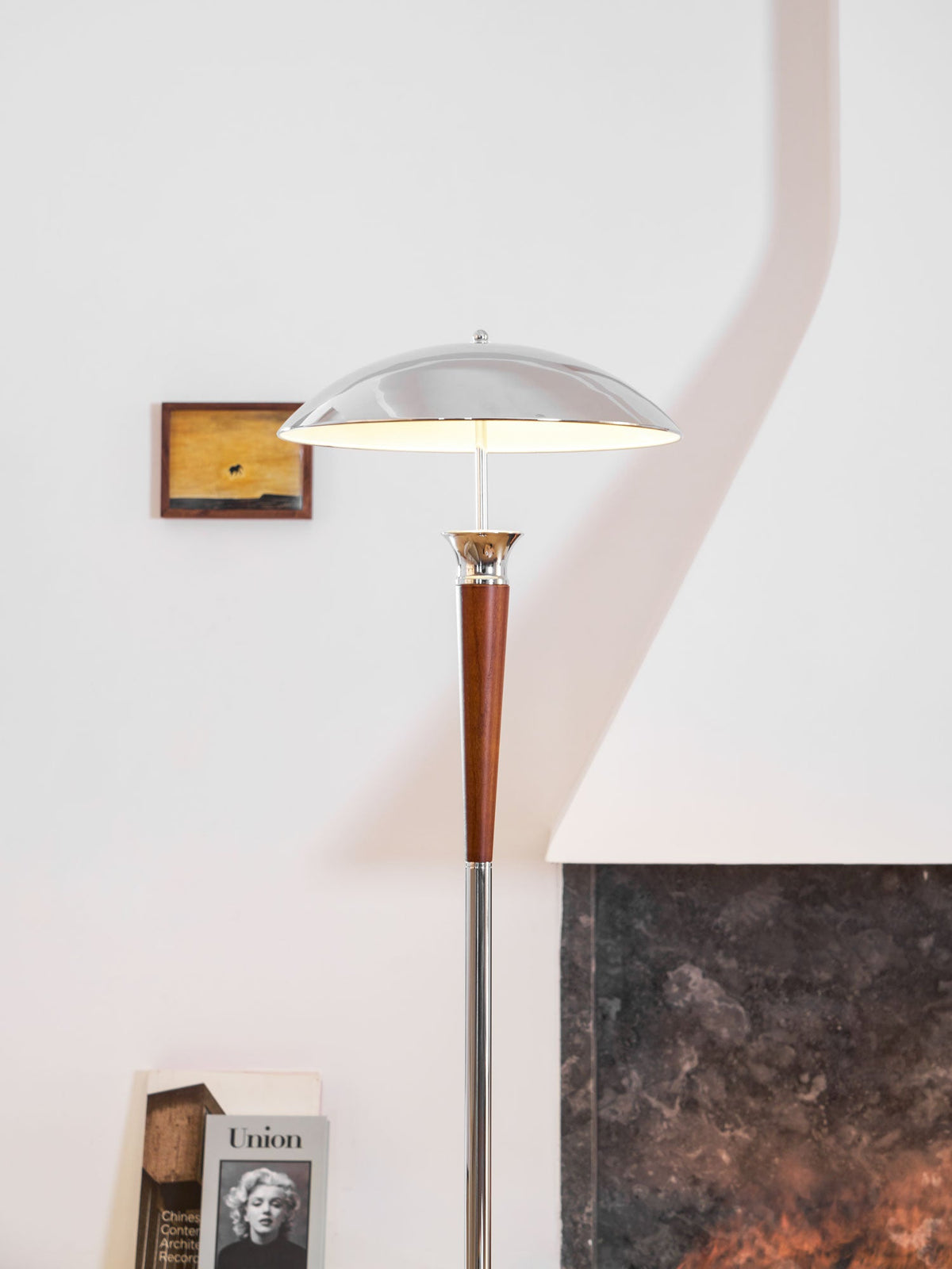 Close view of the walnut stem and chrome pole on this Clérachic floor lamp, with a small frame and a book beside a stone surface.