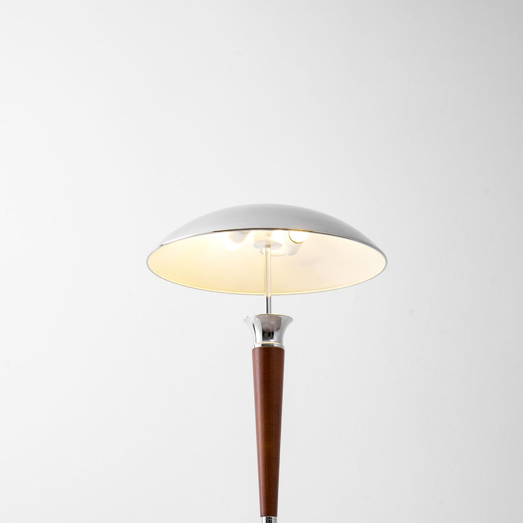 Looking up into the chrome shade of this Clérachic floor lamp, lit warm, with a walnut stem and collar below.