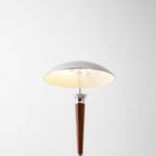 Looking up into the chrome shade of this Clérachic floor lamp, lit warm, with a walnut stem and collar below.