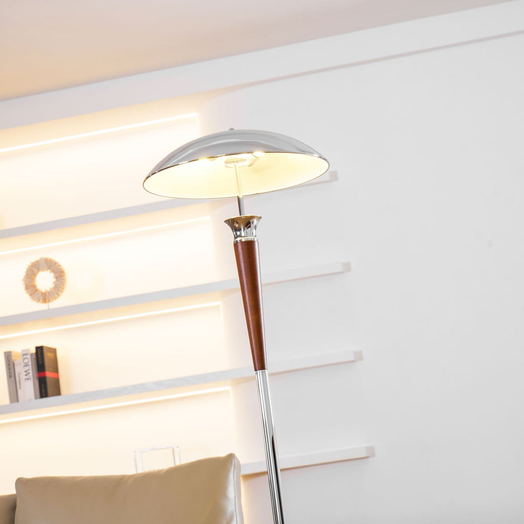 Low view up to the lit chrome shade of this Clérachic floor lamp, with glowing wall shelves and a sofa behind.