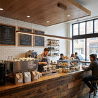 Long walnut bar pendant hung above a timber coffee counter, with chalkboard menus and a tiled wall behind, from Clérachic.