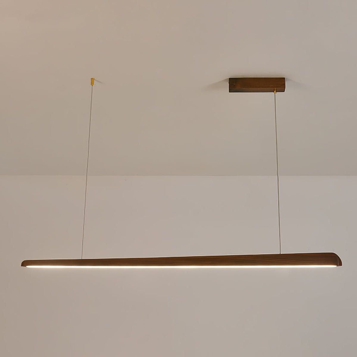 Walnut bar pendant on two thin wires, lit with a neutral white strip along its underside, from Clérachic.