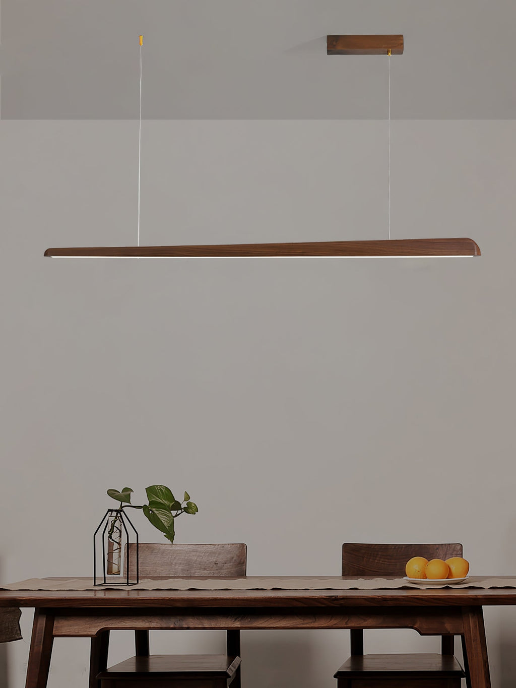Clérachic walnut bar pendant hung above a wooden table set with a small plant and a bowl of oranges.