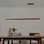 Walnut bar pendant above a wooden table with a glass vase and a plate of oranges, light glowing below, from Clérachic.