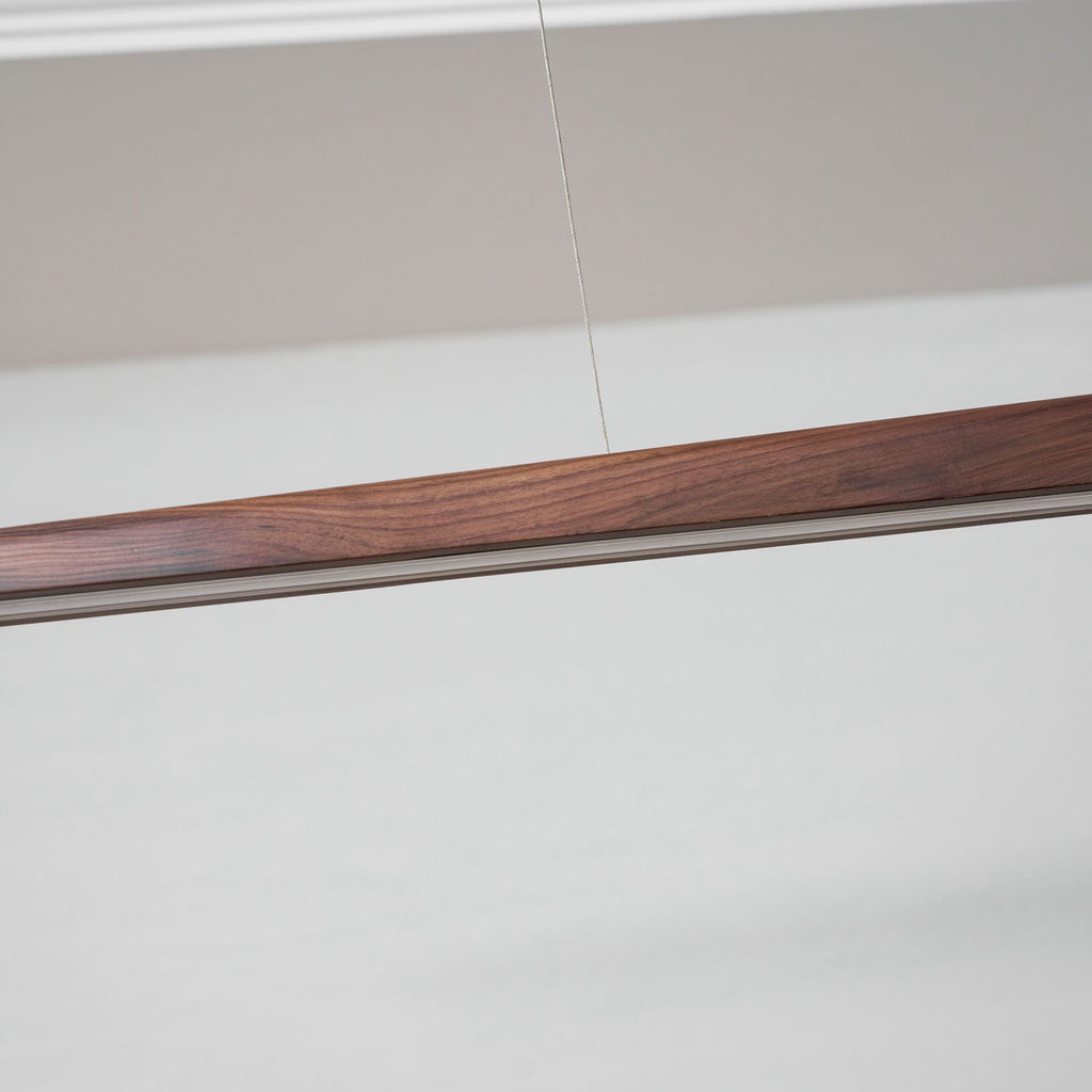 Close view of the walnut grain and the pale diffuser strip along the underside of this Clérachic bar pendant.