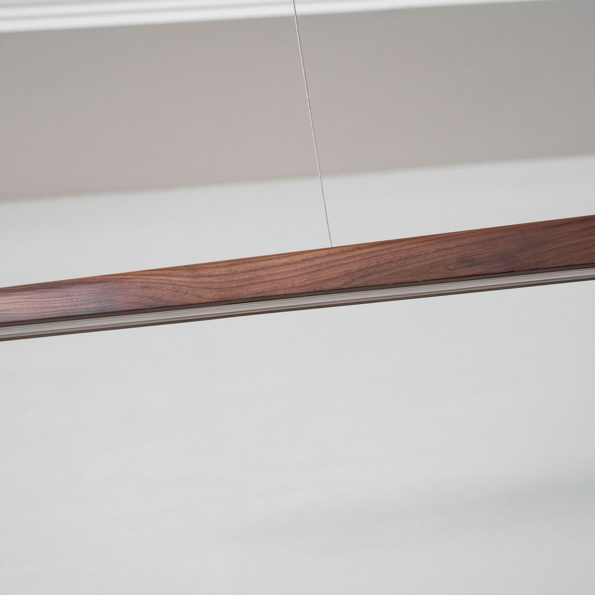 Close view of the walnut grain and the pale diffuser strip along the underside of this Clérachic bar pendant.