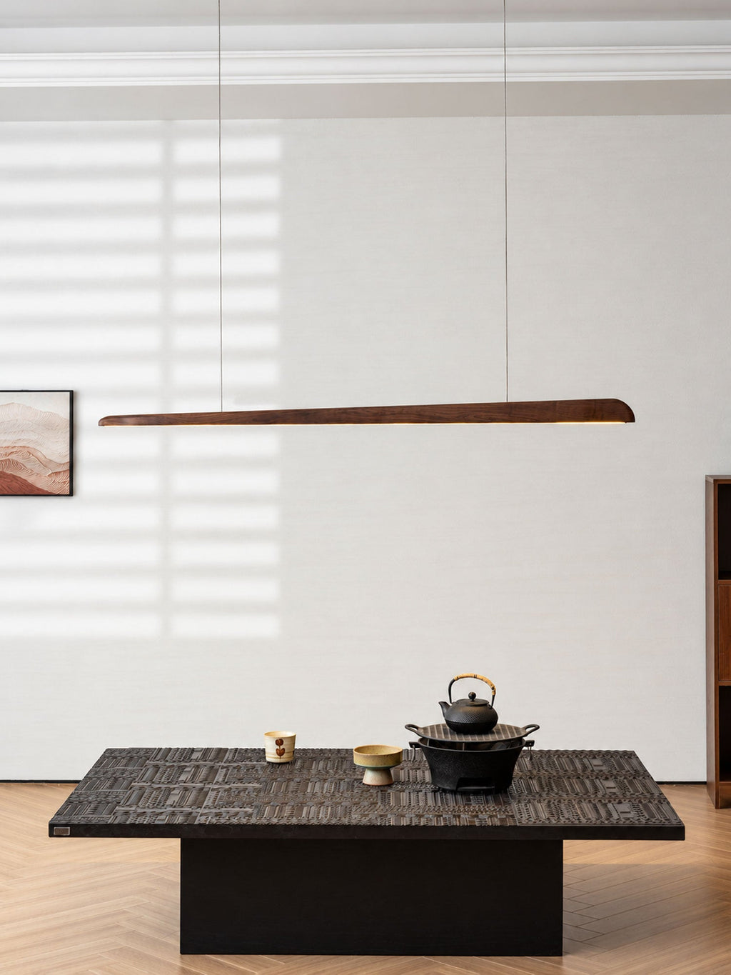 Walnut bar pendant hung against a white wall with window light stripes, above a low black table and an iron teapot, from Clérachic.