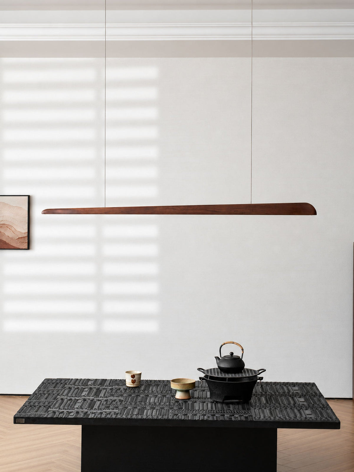 Walnut bar pendant hung against a pale wall with sunlit stripes, a framed print and a low black table, from Clérachic.