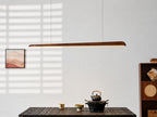 Slim walnut bar pendant above a low black table with an iron teapot, a framed print and a shelf unit beside it, from Clérachic.