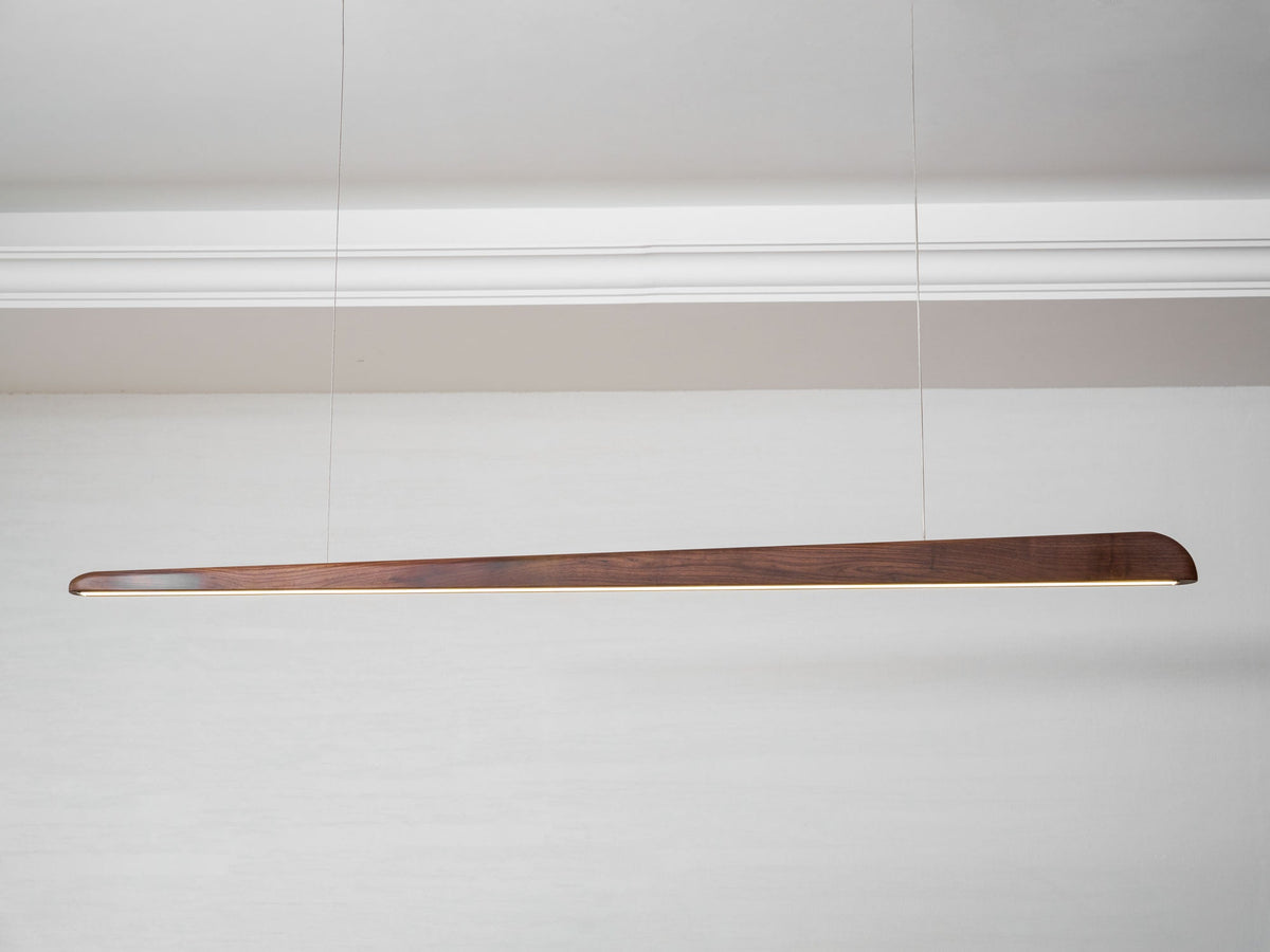 Walnut bar pendant on two thin wires beneath a white cornice, seen from a low angle, from Clérachic.