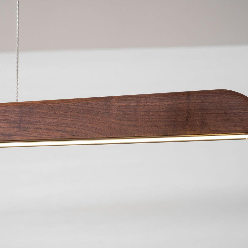Close view of the walnut end and the thin lit strip along the underside of this Clérachic bar pendant.