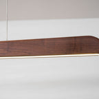 Close view of the walnut end and the thin lit strip along the underside of this Clérachic bar pendant.