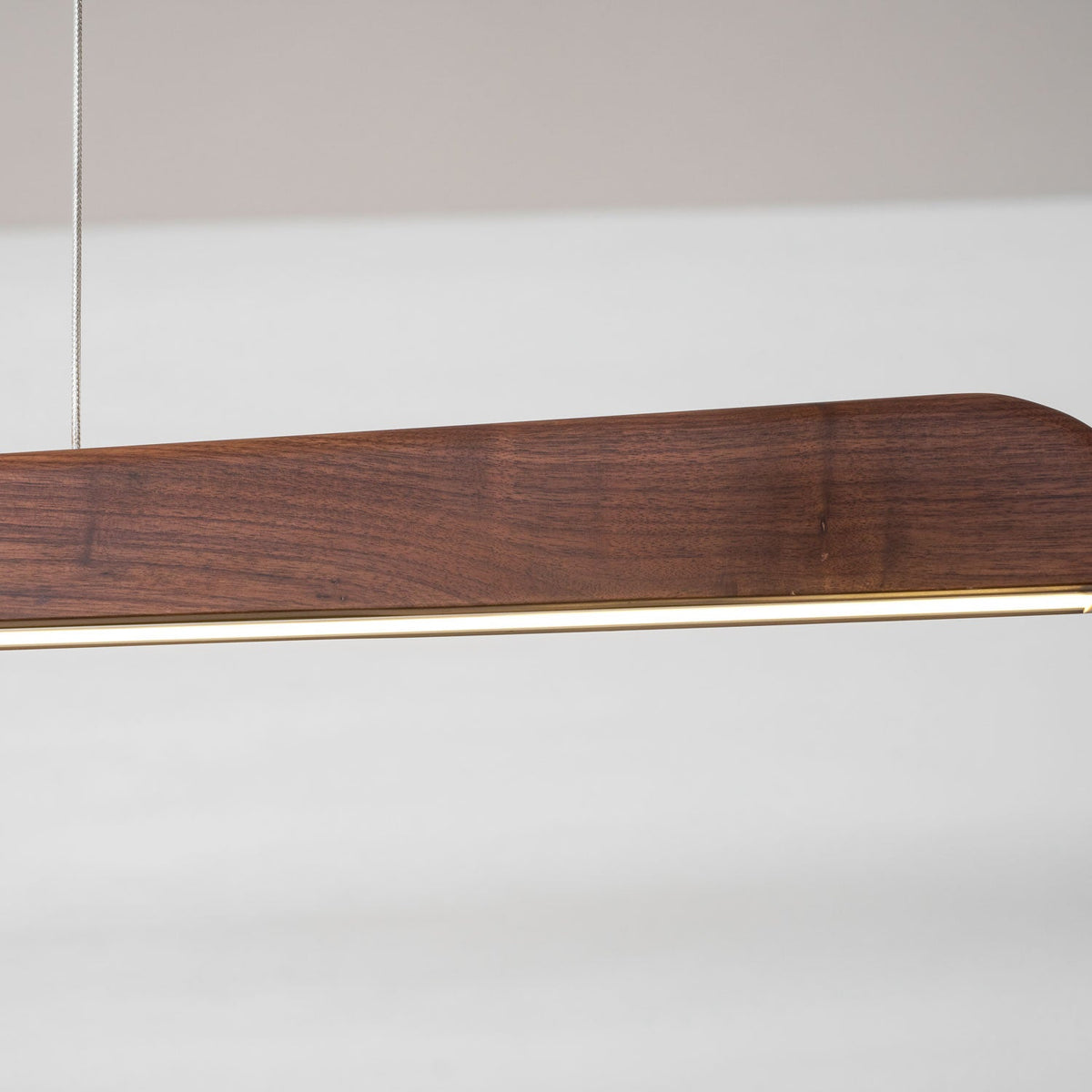 Close view of the walnut end and the thin lit strip along the underside of this Clérachic bar pendant.