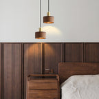 Two of these Clérachic walnut pendants hang at different heights beside a panelled walnut headboard wall, casting a warm pool of light.