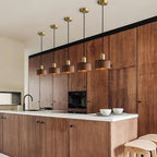 A row of five walnut pendants from Clérachic with brass caps hangs over a kitchen island, in front of walnut cabinets.