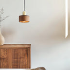 A single Clérachic walnut pendant hangs against a soft cream wall above a walnut sideboard and a pale vase.