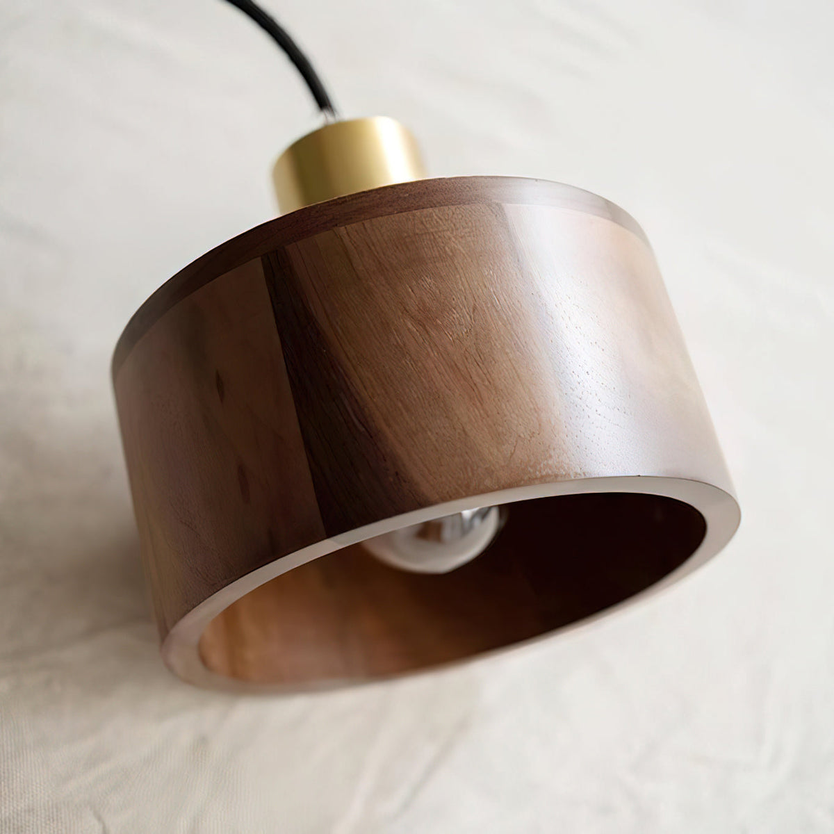Tilted view of this Clérachic walnut shade resting on linen, with the brass cap on top and the bulb just visible inside.
