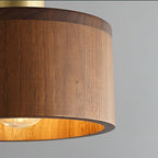 Close view of the walnut grain on this Clérachic pendant, with the bulb glowing and the shade's lit interior golden.