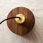 Top view of this Clérachic pendant lying on linen, showing the round walnut top with the brass cap and black cord.
