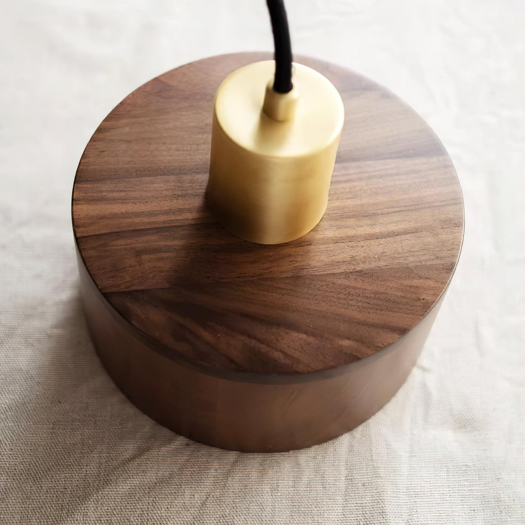 Angled top view of the Clérachic pendant's brass cap sitting on the walnut shade, with the grain running across the lid.