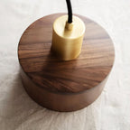 Angled top view of the Clérachic pendant's brass cap sitting on the walnut shade, with the grain running across the lid.