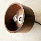 Side-on view into the open walnut shade of this Clérachic pendant, with a clear bulb visible on its holder inside.