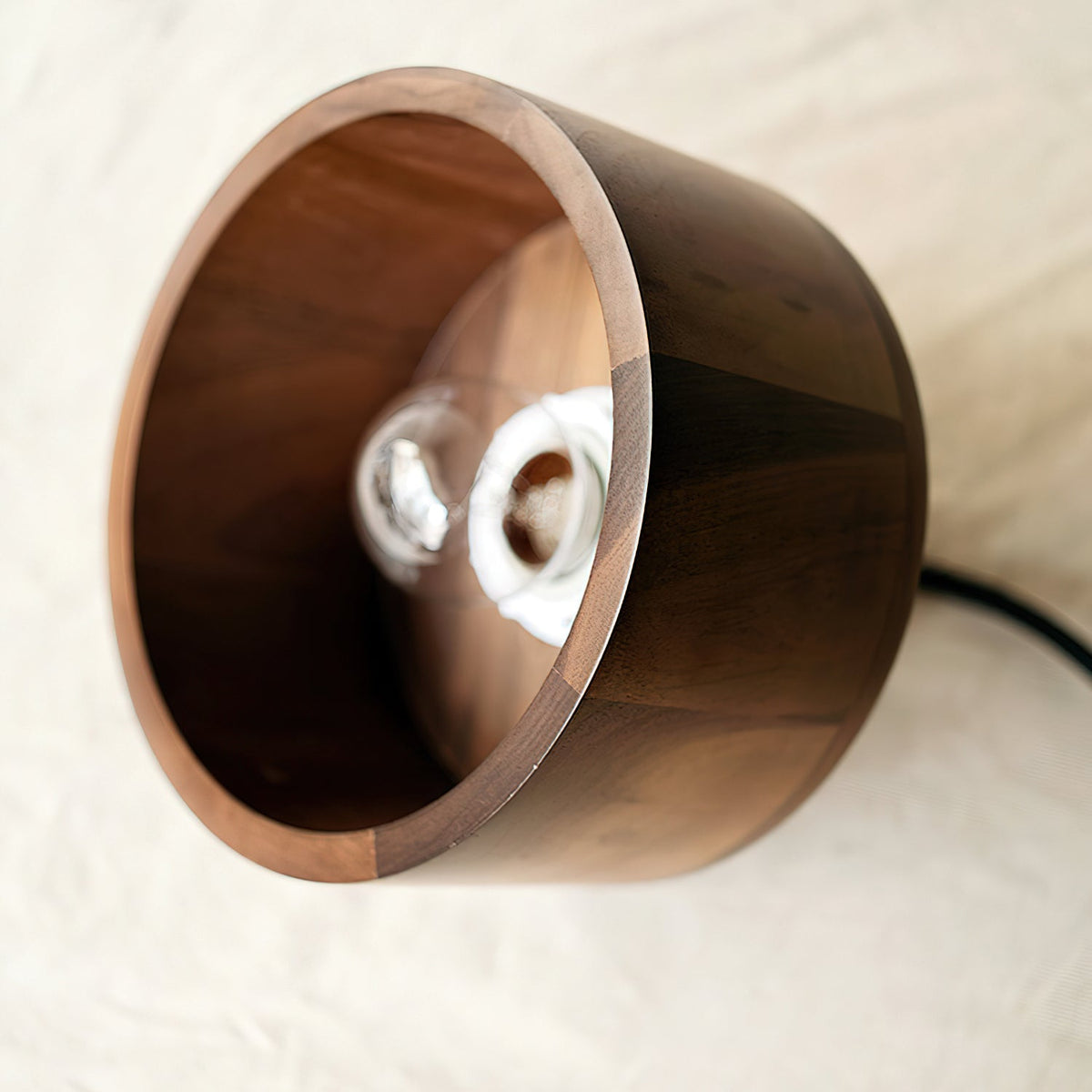 Side-on view into the open walnut shade of this Clérachic pendant, with a clear bulb visible on its holder inside.