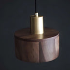 A brass cap above the flat walnut top of this Clérachic pendant, photographed against a dark charcoal backdrop.