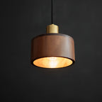 Lit from within, this Clérachic walnut pendant throws warm light from its open base against a dark backdrop.