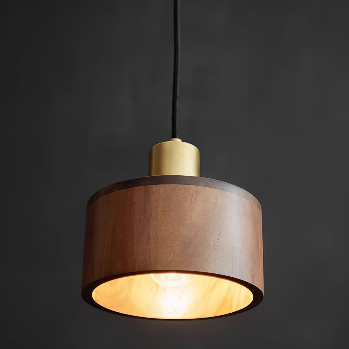 This Clérachic pendant glows warm amber inside its walnut shade, with the bulb just visible, on a dark grey background.