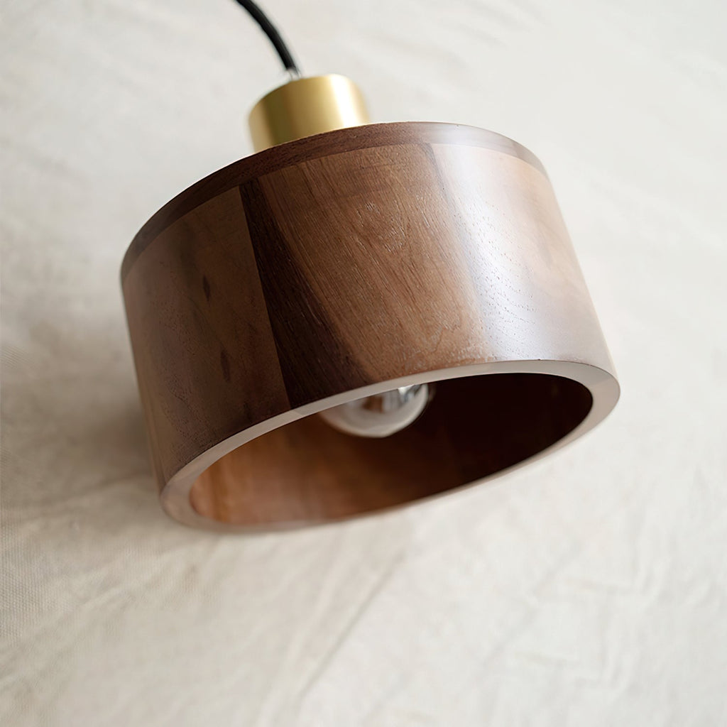 A Clérachic walnut pendant tipped on its side on linen, showing the layered wood rim and a bulb inside.