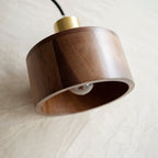 A Clérachic walnut pendant tipped on its side on linen, showing the layered wood rim and a bulb inside.
