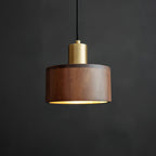 Front view of this Clérachic pendant with a brass cap and a walnut shade, its rim lit softly from below, on a dark backdrop.