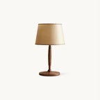 Cut-out view of a Clérachic table lamp with a beige linen shade stitched at the edges and a turned walnut-colour stem on a round base.