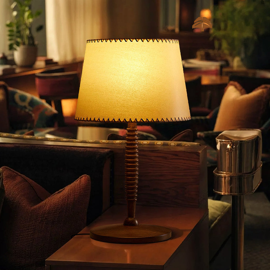 Close view of the lit beige shade and turned walnut-colour stem of this Clérachic table lamp, on a dark wood side table.