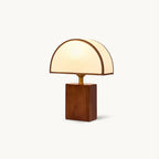 A Clérachic table lamp with a half-round white fabric shade and a walnut block base with a brass neck, on a white backdrop.