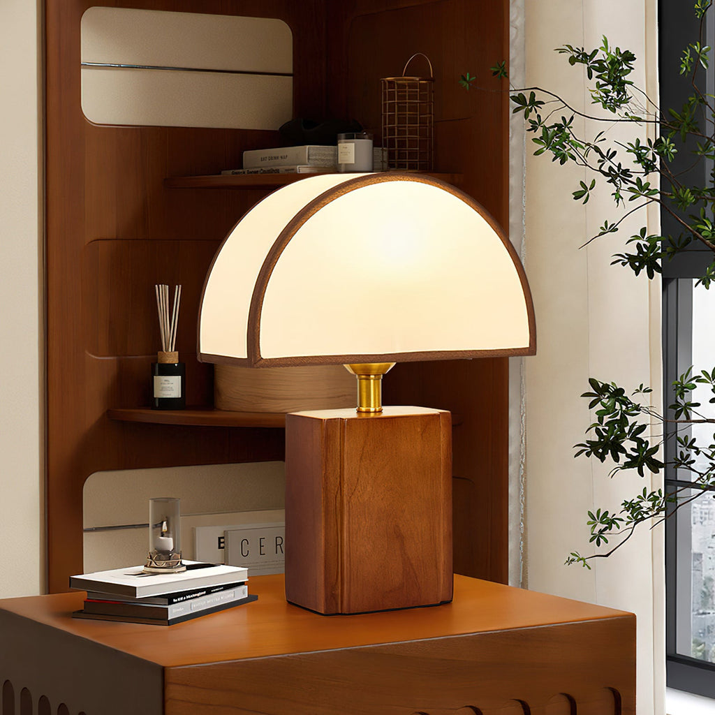 Close, low view of a lit Clérachic table lamp with a half-round shade, on a walnut cabinet with books and a reed diffuser.