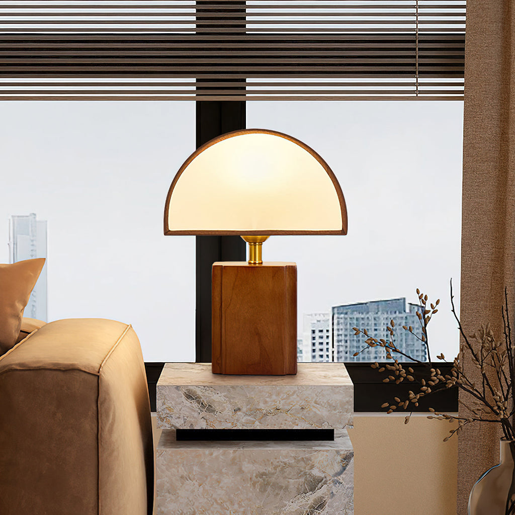 Clérachic table lamp with a half-round fabric shade on a stone side table, between a tan armchair and a city-view window.