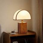 A Clérachic table lamp with a walnut base and half-round white shade, on a bedside cabinet against a warm beige wall.