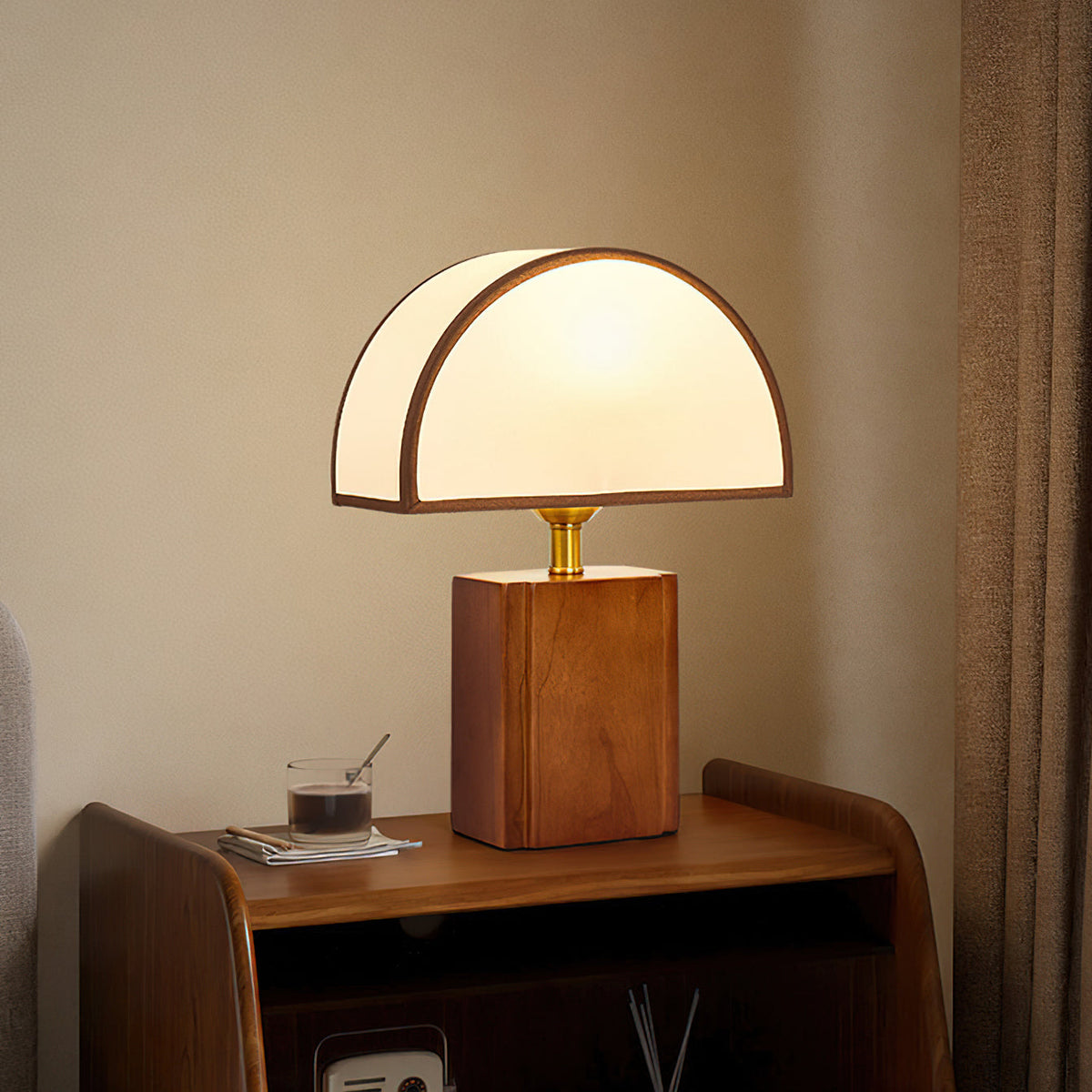 A Clérachic table lamp with a walnut base and half-round white shade, on a bedside cabinet against a warm beige wall.