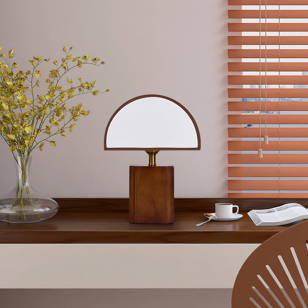 Clérachic table lamp with a half-round white shade on a dark wooden desk, beside a coffee cup, a book and a vase of yellow flowers.