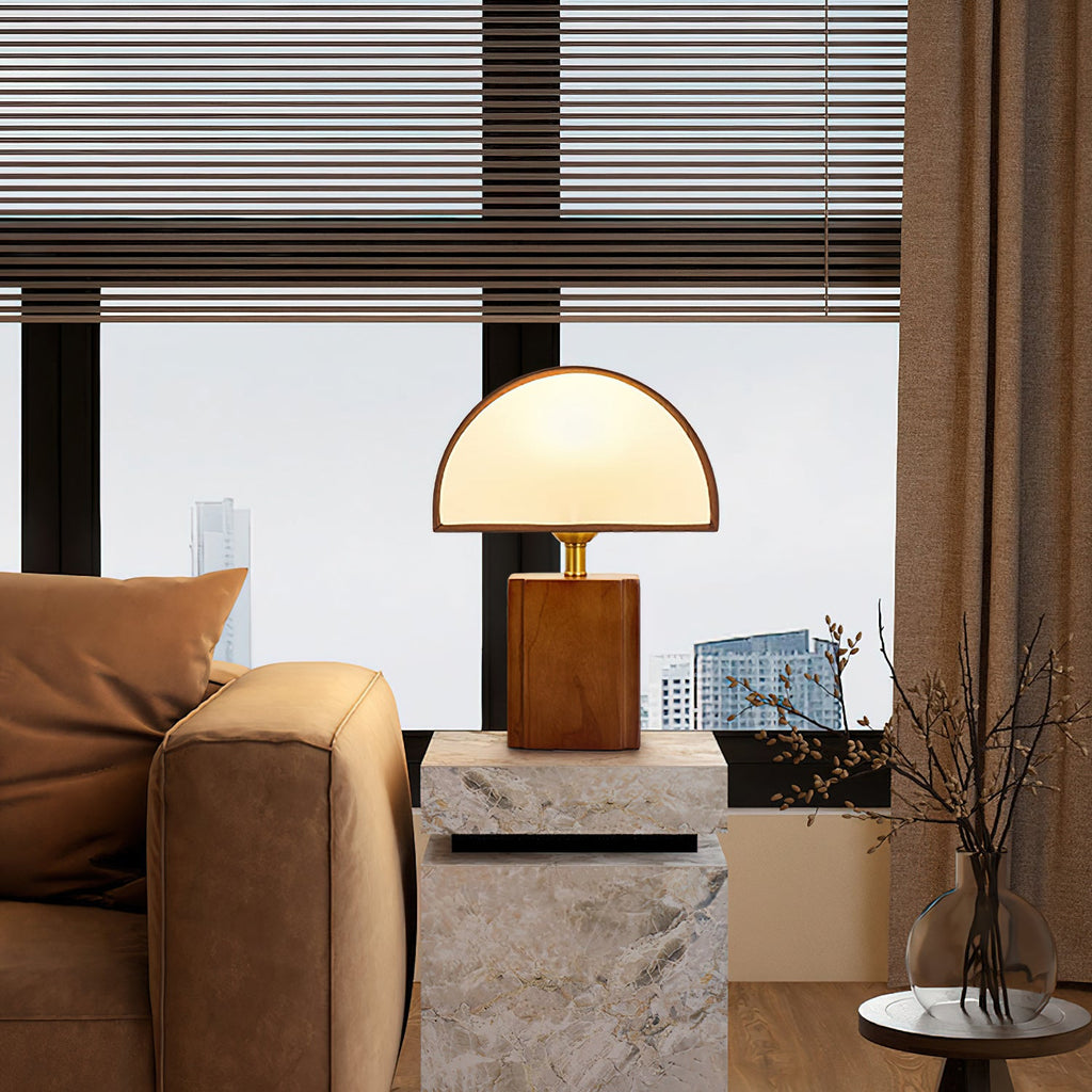 A Clérachic table lamp on a stone side table by a tan sofa arm, with a window and a city skyline behind it.