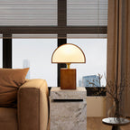 A Clérachic table lamp on a stone side table by a tan sofa arm, with a window and a city skyline behind it.