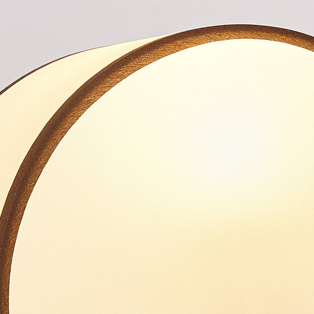 Close view of the half-round white fabric shade and its dark piped edge on this Clérachic table lamp.