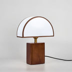 Seen from the front on a pale grey backdrop, a Clérachic table lamp with a half-round white shade and its cord trailing right.